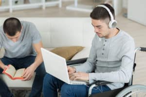 Man reading book, disabled friend using laptop
